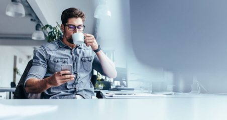 A man drinking coffee and using mobile phone in the office