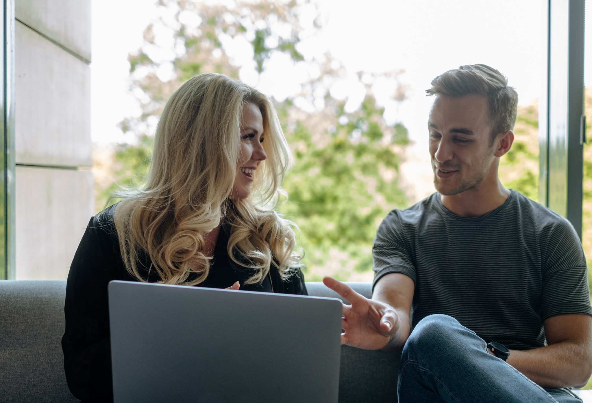 a man and a woman sitting on a couch and looking at the laptop screen in an office space