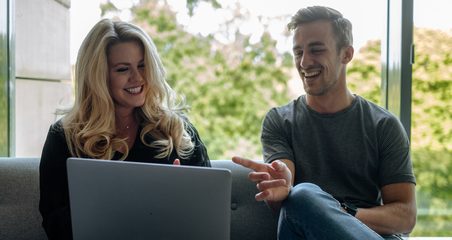 a man and a woman sitting on a couch and looking at the laptop screen in an office space