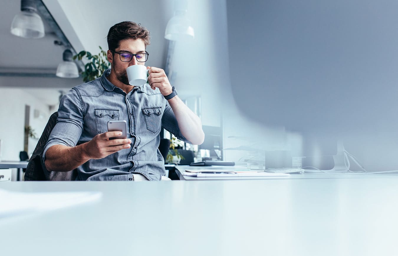 A man drinking coffee and using mobile phone in the office