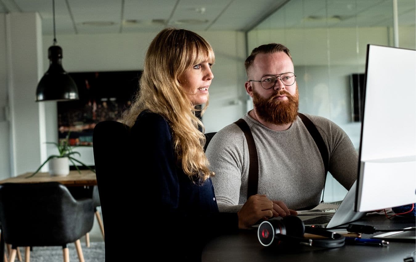 two coworkers sitting at a desk looking at a computer
