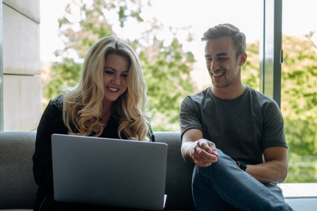 two employees smiling in front of a laptop in an open office space