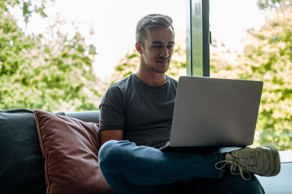 Male employee sat on a couch and taking online compliance training by using his laptop