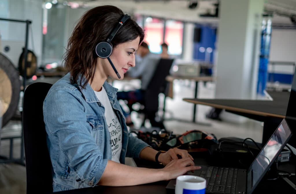 woman working in front of a laptop with headphones in open office space